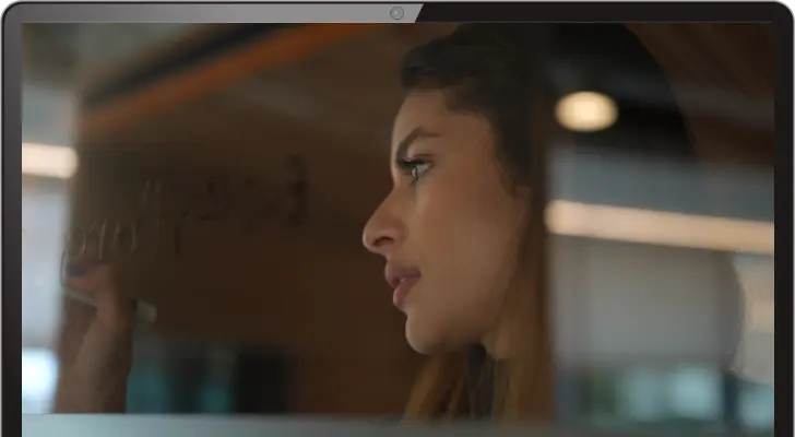 A woman writing something on a clear glass board.